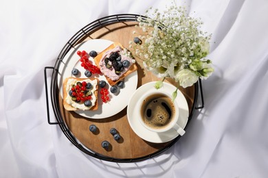 Tray with cup of coffee, cream cheese sandwiches and flowers on white fabric, top view