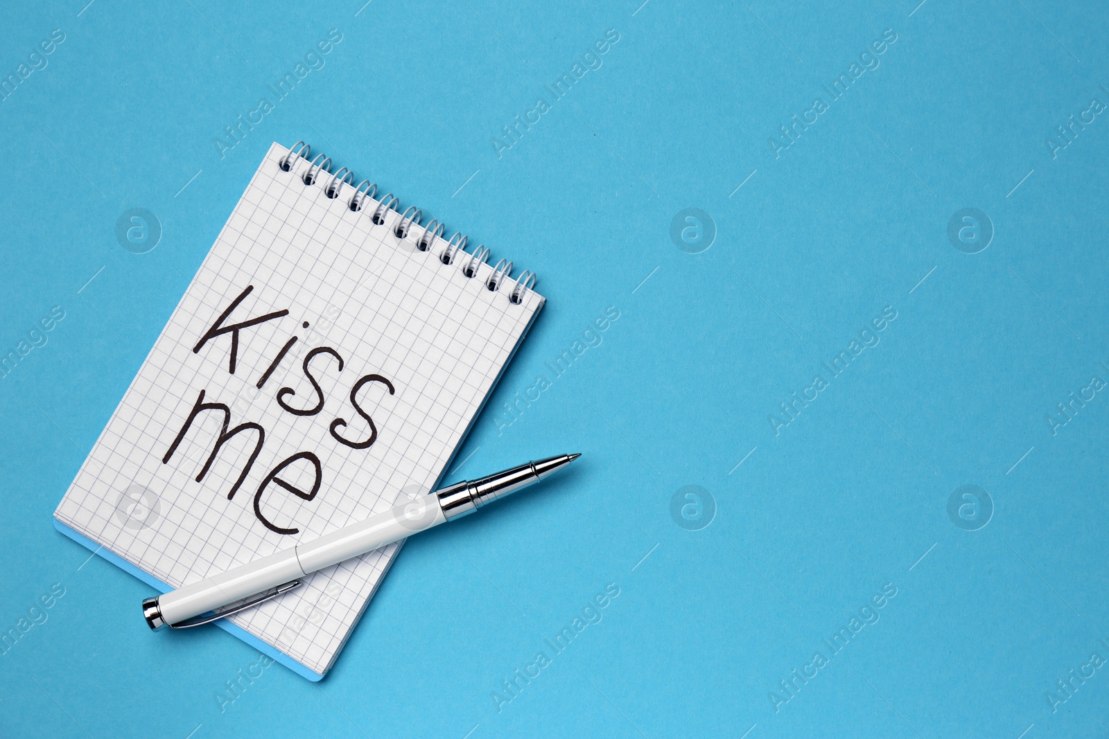 Photo of Notebook with phrase Kiss me and pen on light blue background, top view. Space for text