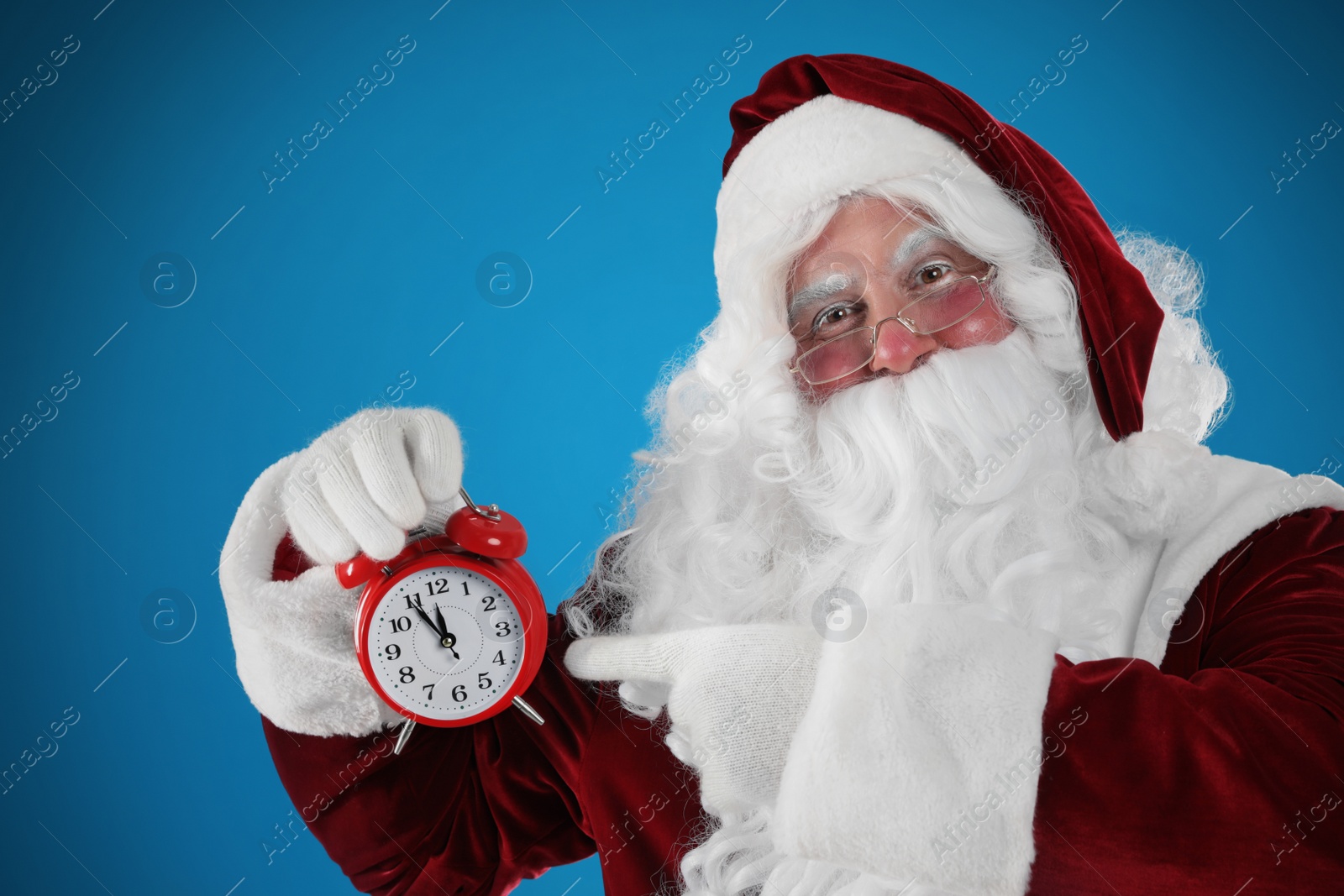 Photo of Santa Claus holding alarm clock on blue background. Christmas countdown