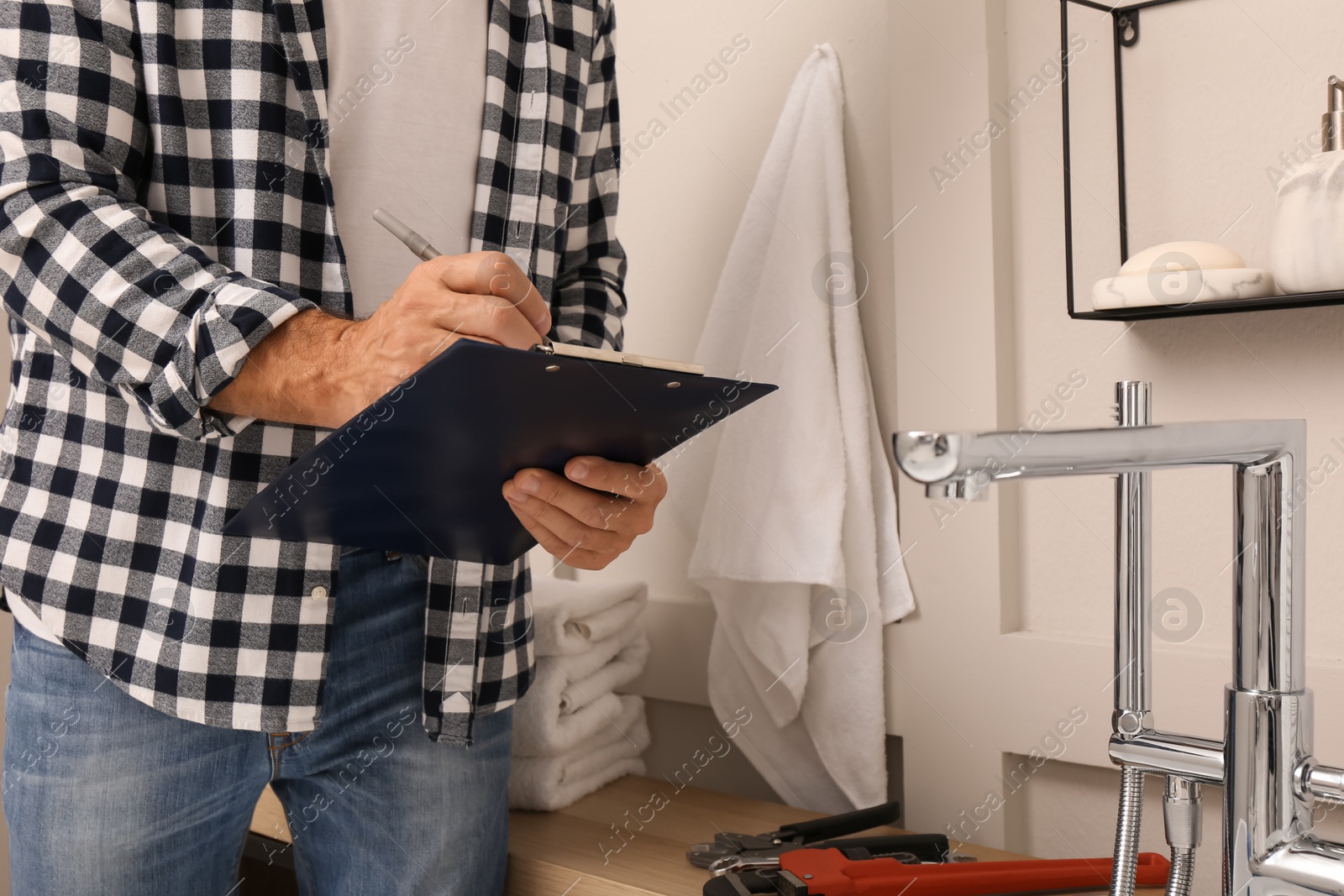 Photo of Plumber with clipboard checking water tap in bathroom, closeup