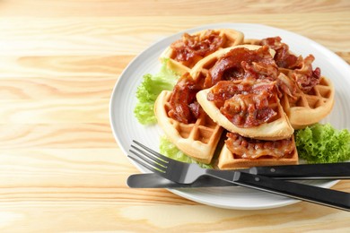 Photo of Tasty Belgian waffles served with bacon and lettuce on wooden table, closeup. Space for text