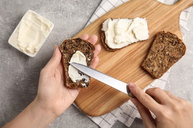 Photo of Woman spreading cream cheese onto bread at grey table, closeup