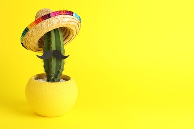 Photo of Cactus with Mexican sombrero hat and fake mustache on yellow background, space for text