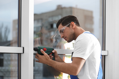 Photo of Construction worker repairing plastic window with electric screwdriver indoors