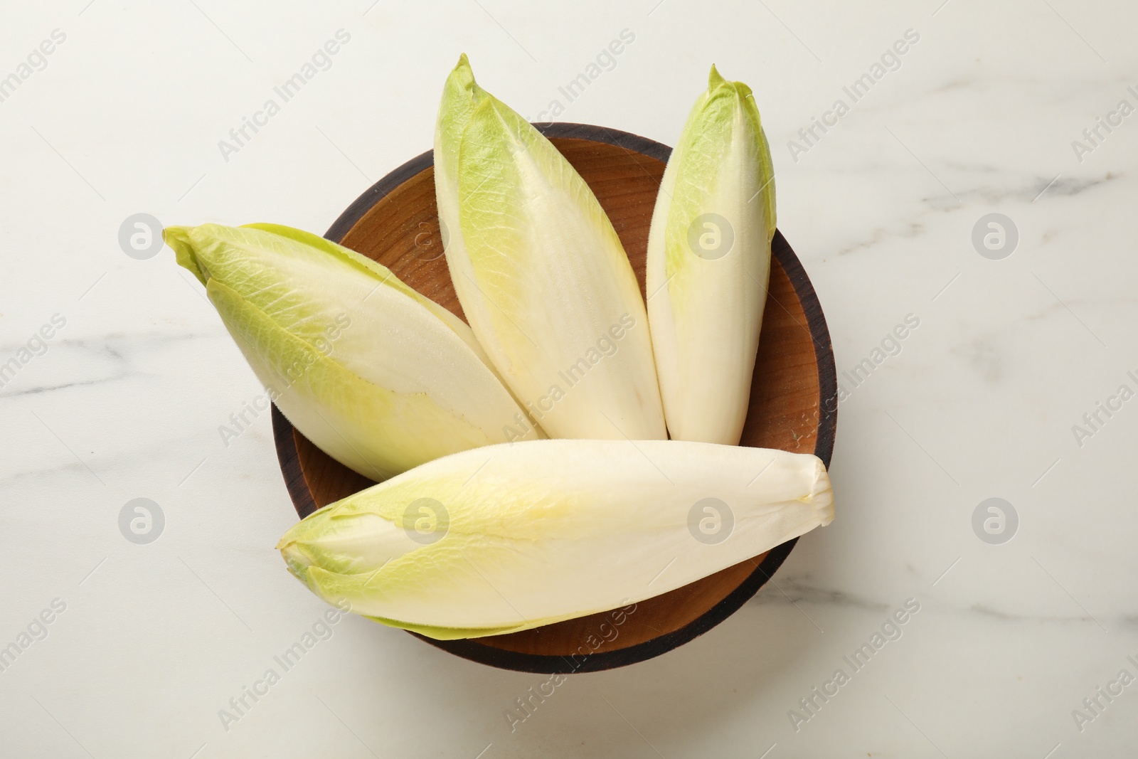 Photo of Raw ripe chicories in bowl on white marble table, top view