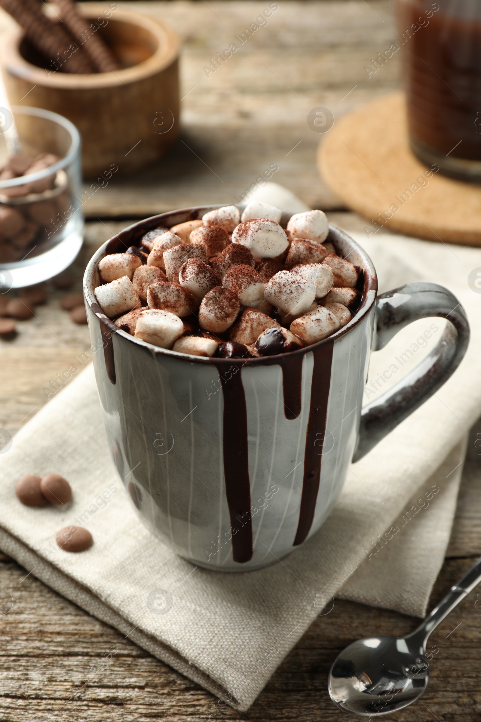 Photo of Delicious hot chocolate with marshmallows and cocoa powder in cup on wooden table