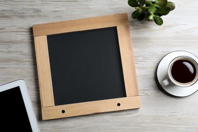 Photo of Clean small chalkboard, coffee, plant and tablet on light wooden table, flat lay