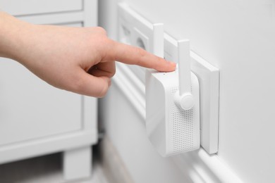 Woman turning on wireless Wi-Fi repeater indoors, closeup