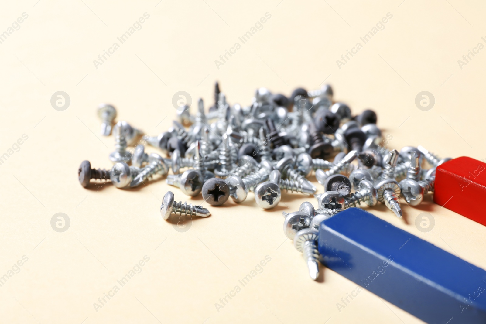 Photo of Magnet attracting screws on beige background, closeup