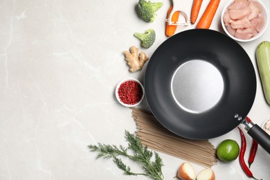 Photo of Empty iron wok surrounded by raw ingredients on light table, flat lay. Space for text