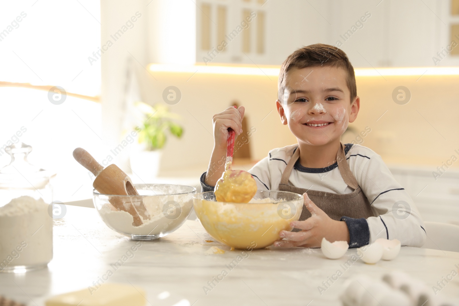 Photo of Cute little boy cooking dough at table in kitchen