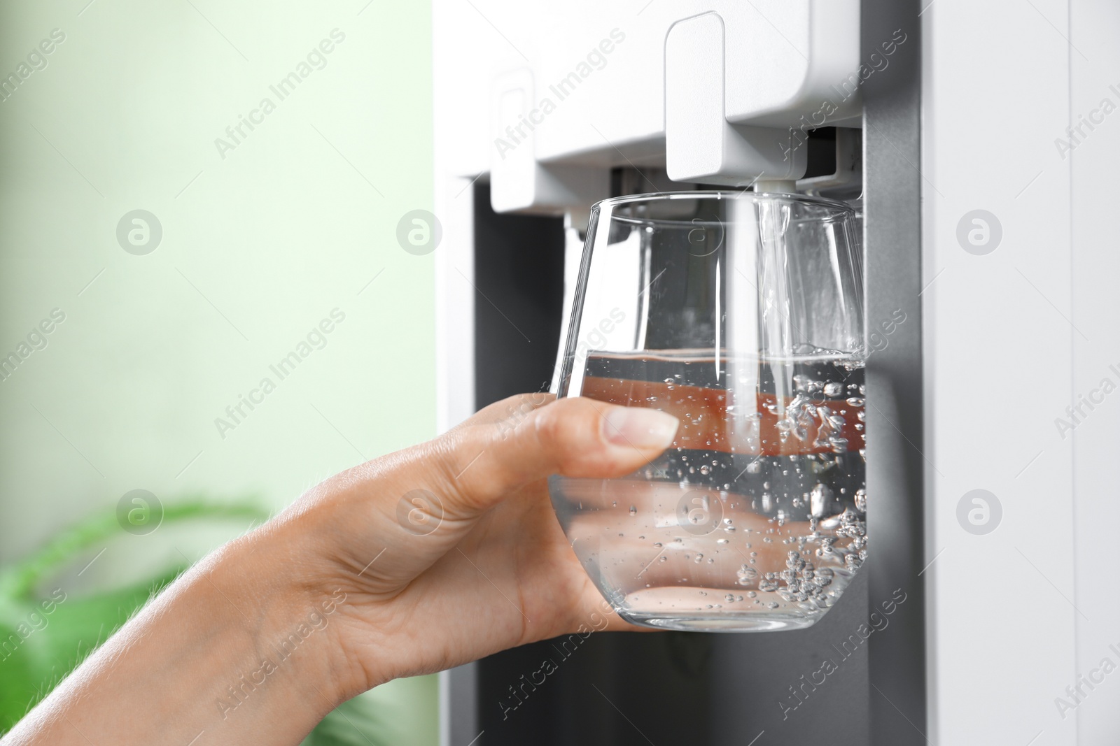 Photo of Woman filling glass from water cooler indoors, closeup. Refreshing drink