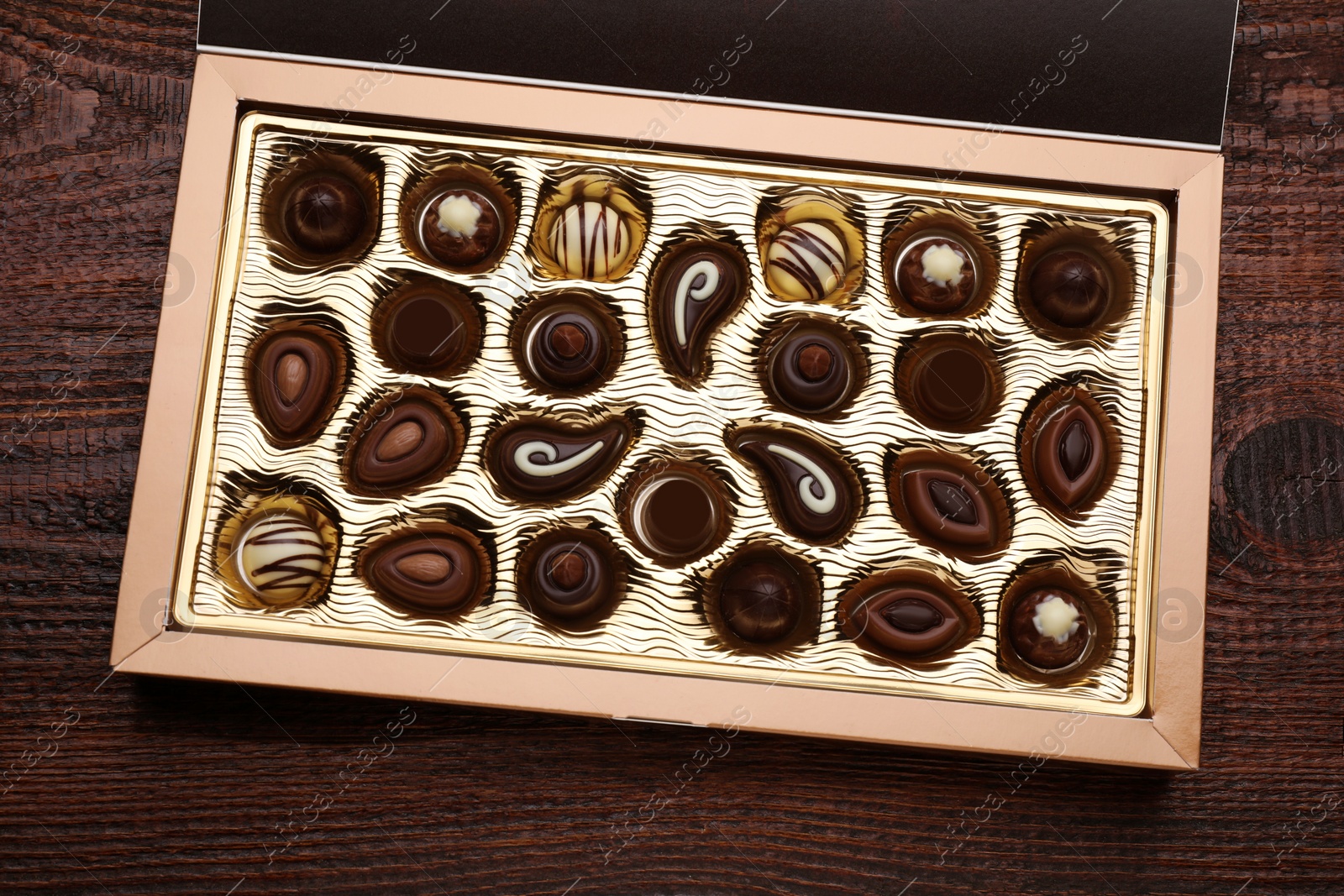 Photo of Box of delicious chocolate candies on wooden table, top view