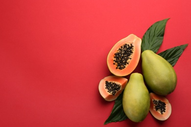 Fresh ripe papaya fruits with green leaves on red background, flat lay. Space for text