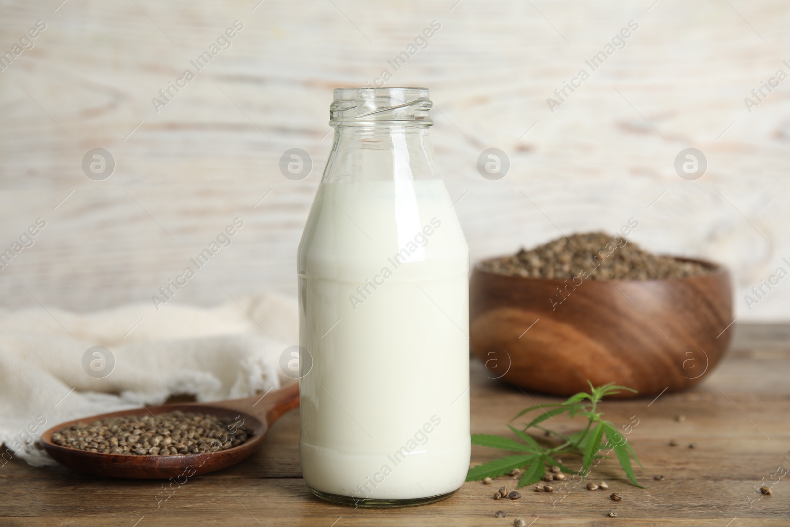 Photo of Glass bottle of hemp milk, seeds and leaves on wooden table