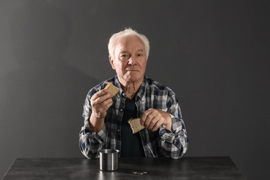 Photo of Poor elderly man with bread at table against dark background