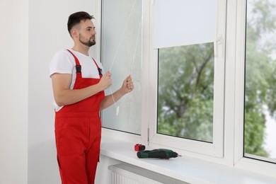 Worker in uniform opening roller window blind indoors