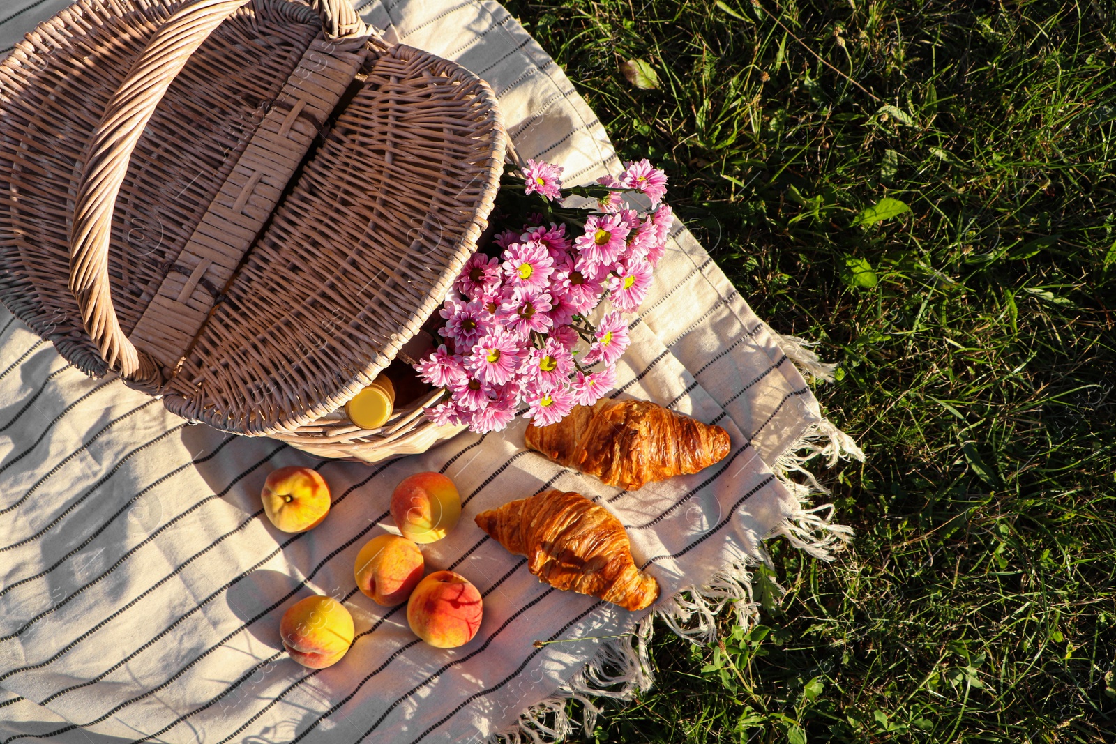 Photo of Picnic basket with flowers, bottle of wine and food on blanket outdoors, top view