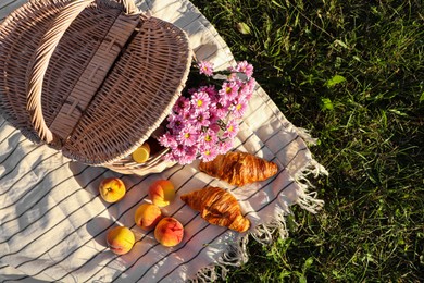 Picnic basket with flowers, bottle of wine and food on blanket outdoors, top view