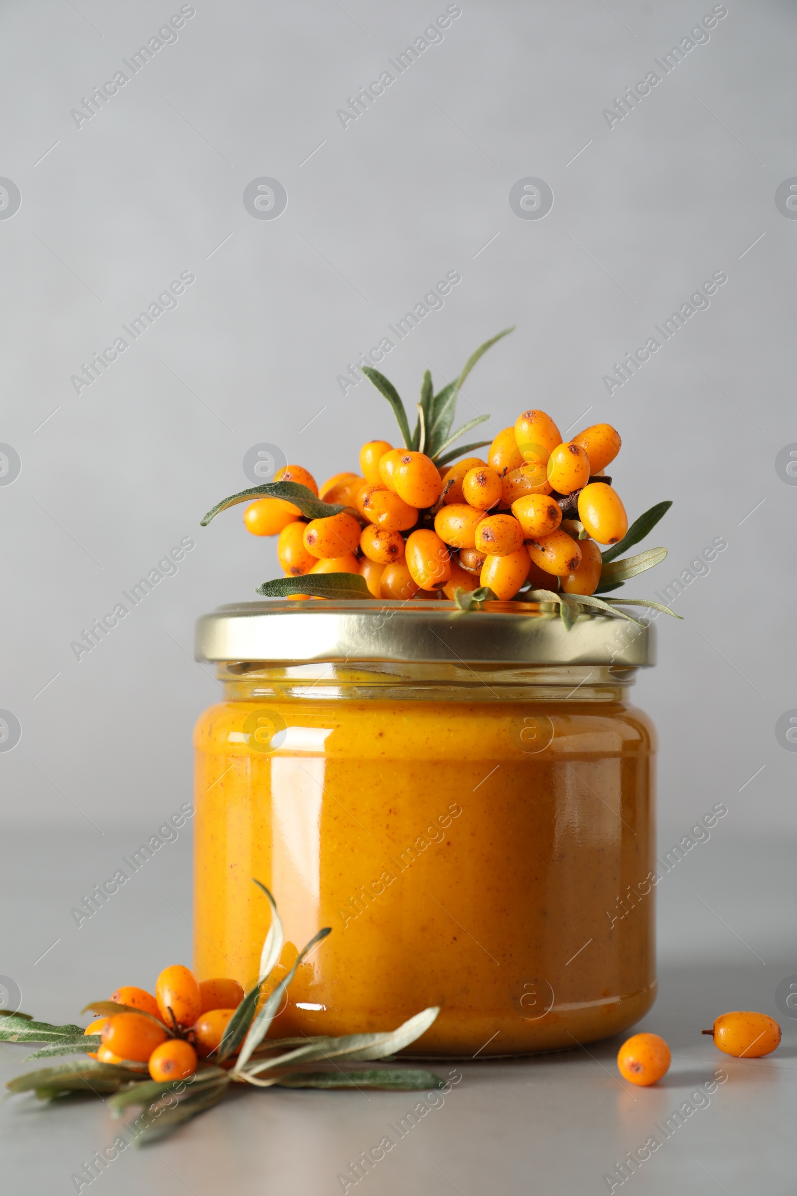 Photo of Delicious sea buckthorn jam and fresh berries on grey table