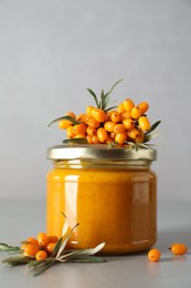 Delicious sea buckthorn jam and fresh berries on grey table