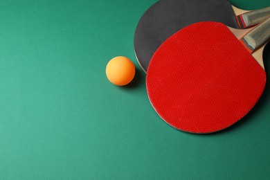 Photo of Ping pong ball and rackets on green background, flat lay. Space for text