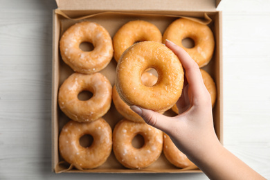 Photo of Woman holding delicious donut at white wooden table, top view