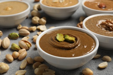 Photo of Tasty nut butters in bowls and raw nuts on light grey table, closeup