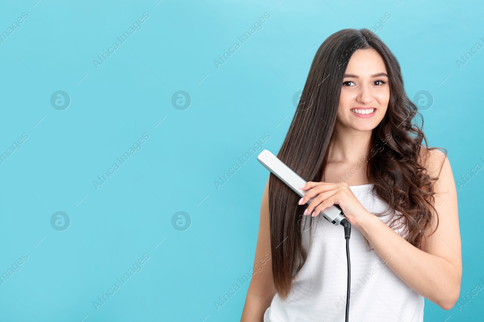 Photo of Young woman using hair iron on blue background, space for text