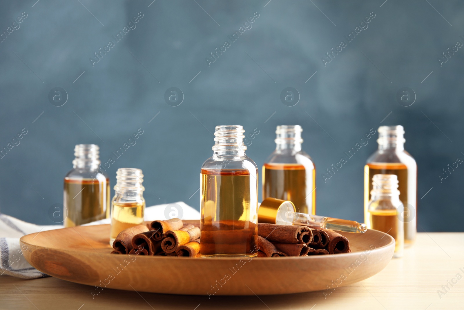 Photo of Bottles of essential oils and cinnamon sticks on table against blue background