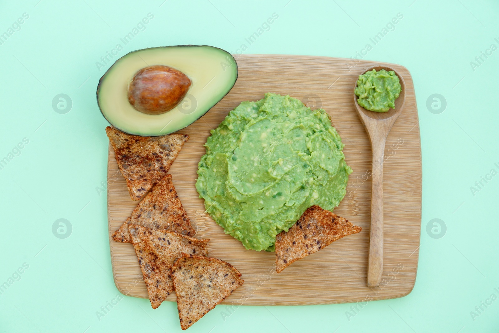 Photo of Delicious guacamole made of avocados, nachos and cut fruit on color background, top view