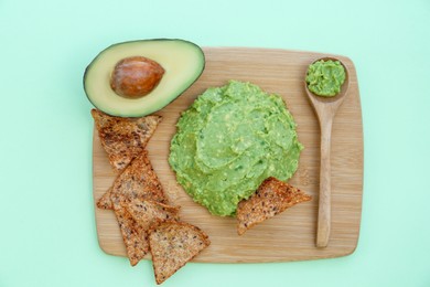 Delicious guacamole made of avocados, nachos and cut fruit on color background, top view