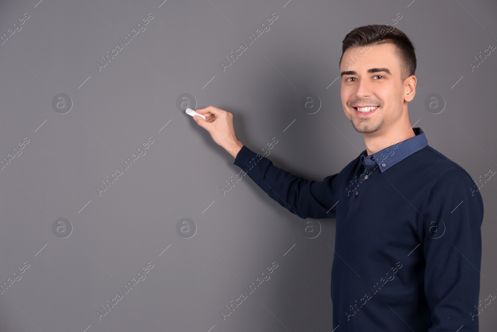 Photo of Young male teacher with chalk on grey background