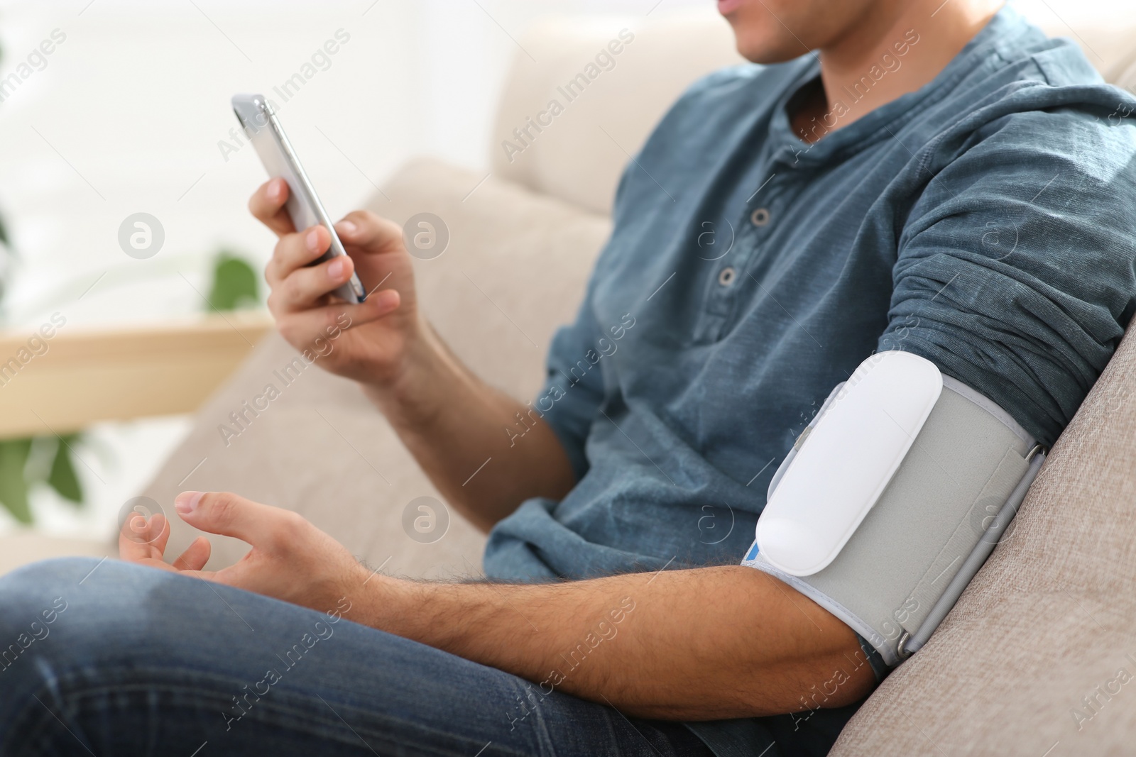 Photo of Man checking blood pressure with modern monitor and smartphone indoors, closeup