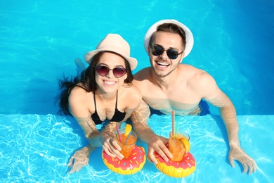 Photo of Young couple with refreshing cocktails in swimming pool on sunny day