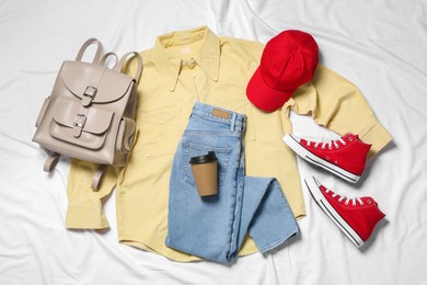 Pair of stylish red shoes, clothes and backpack on white fabric, flat lay