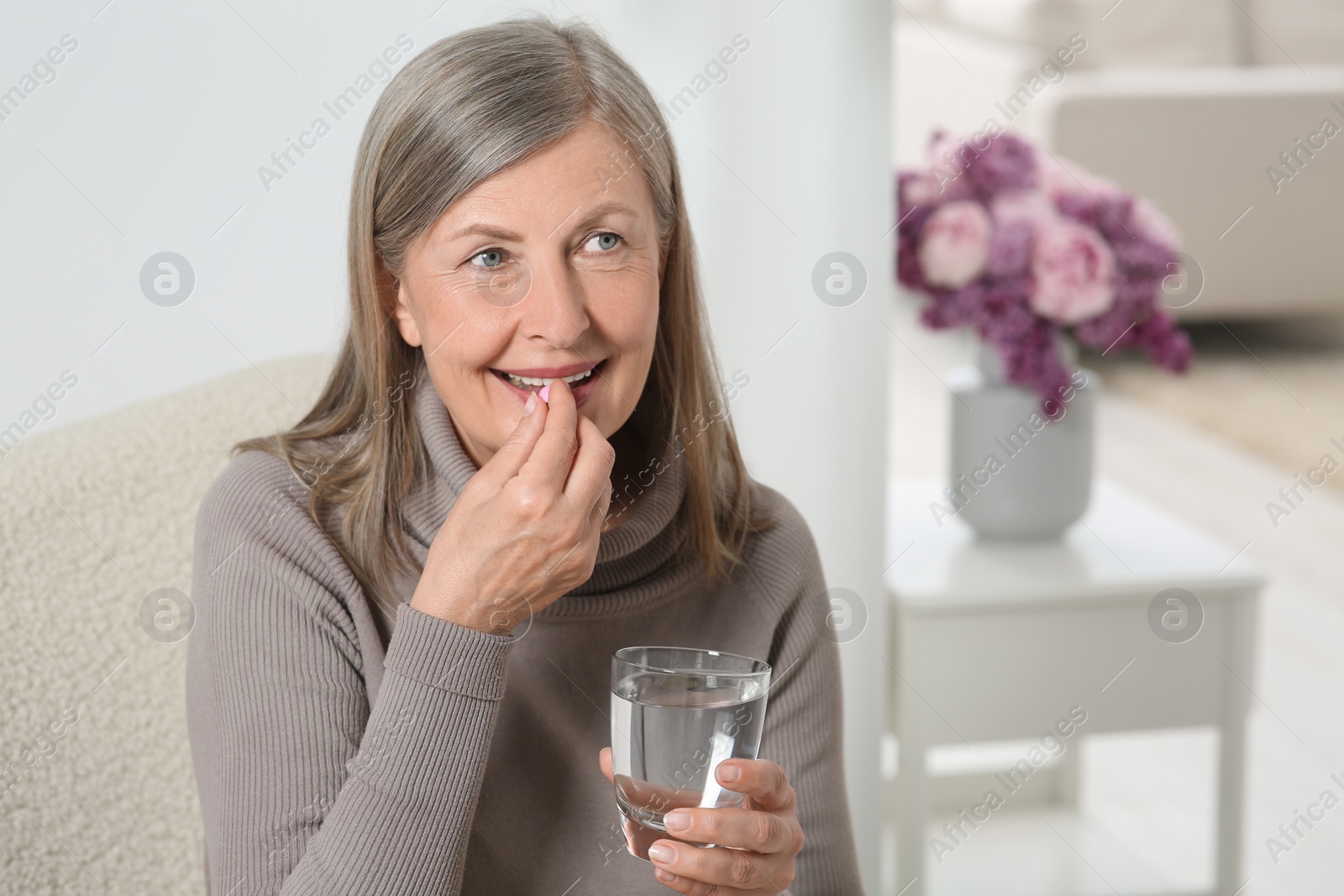 Photo of Senior woman with glass of water taking pill at home. Space for text