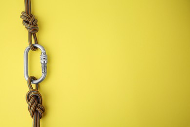 Photo of One metal carabiner with ropes on yellow background, top view. Space for text