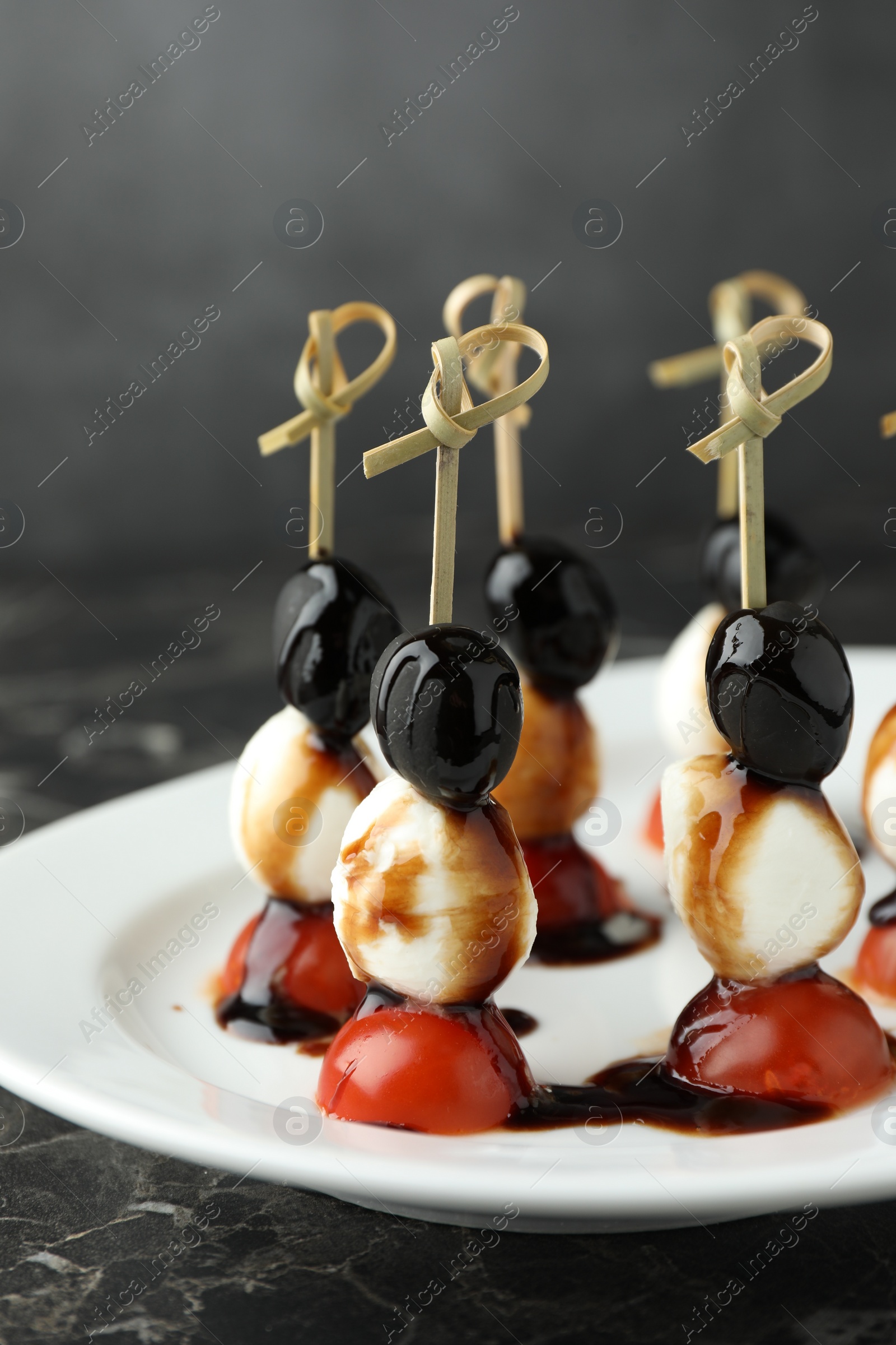 Photo of Tasty canapes with black olives, mozzarella and cherry tomatoes on dark textured table, closeup