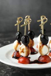 Photo of Tasty canapes with black olives, mozzarella and cherry tomatoes on dark textured table, closeup
