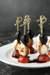 Tasty canapes with black olives, mozzarella and cherry tomatoes on dark textured table, closeup