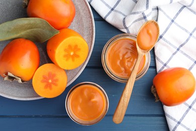 Photo of Delicious persimmon jam in glass jars served on blue wooden table, flat lay