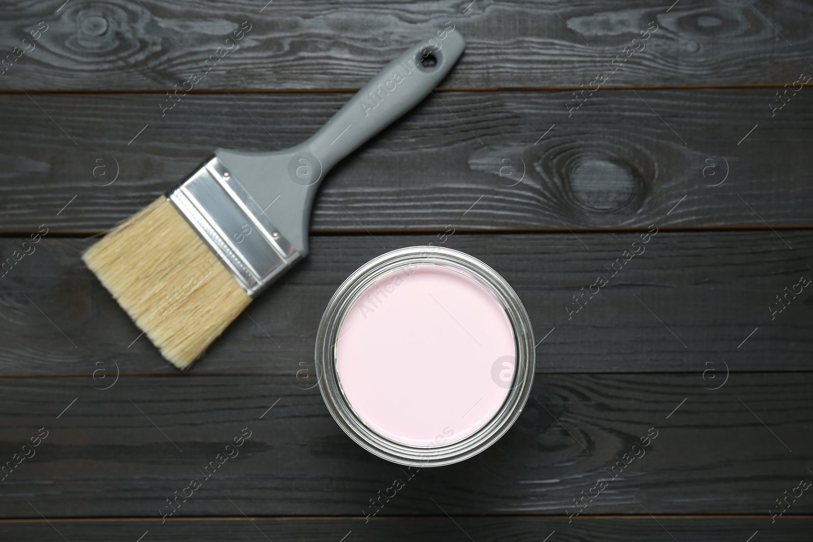 Photo of Can of pale pink paint and brush on black wooden table, flat lay