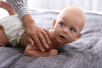 Young woman massaging cute little baby on bed at home