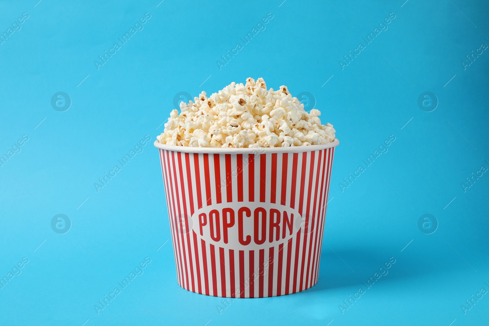 Photo of Delicious popcorn in paper bucket on light blue background