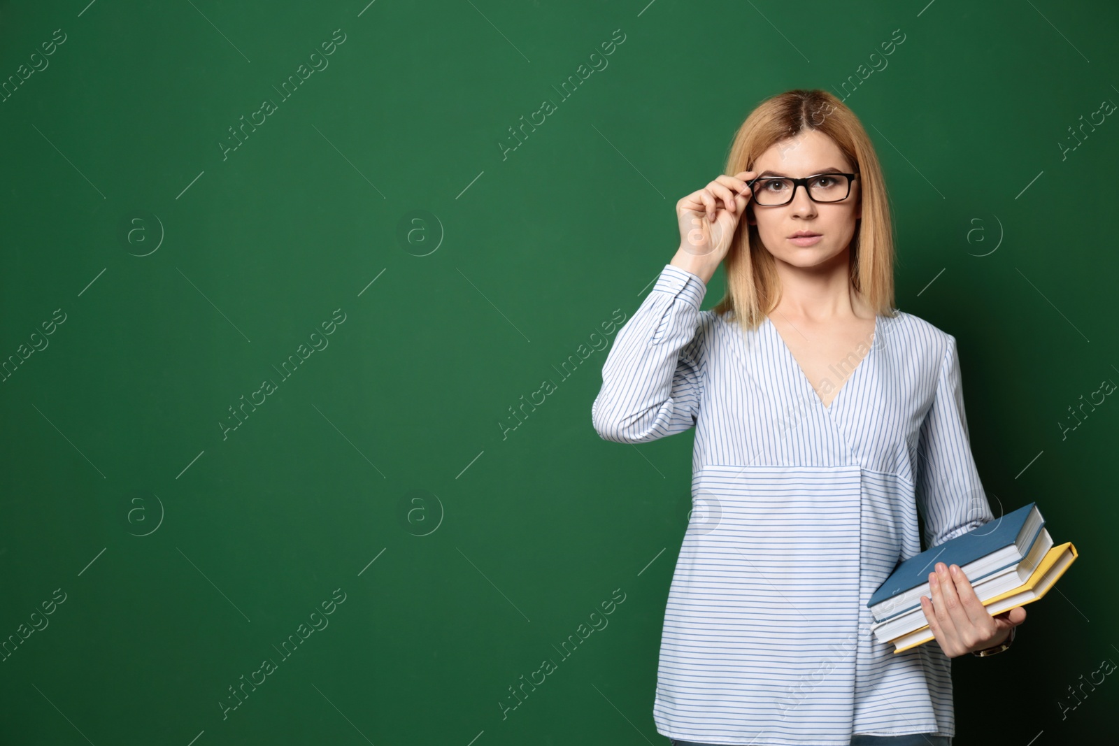 Photo of Portrait of beautiful teacher with books near chalkboard, space for text