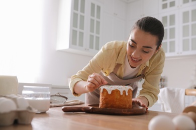 Photo of Young woman decorating traditional Easter cake with sprinkles in kitchen, space for text