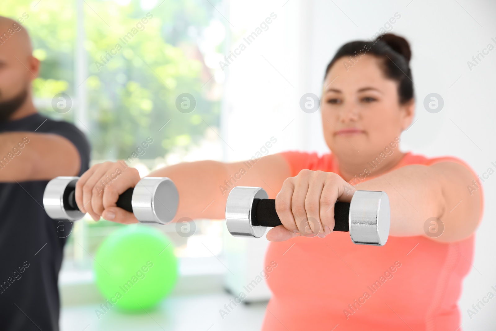 Photo of Overweight man and woman doing exercise with dumbbells in gym