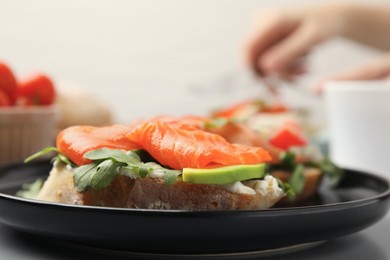 Photo of Tasty bruschetta with salmon, arugula and avocado on black plate, closeup