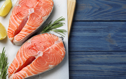 Photo of Top view of fresh raw salmon with lemon and rosemary on blue wooden table, space for text. Fish delicacy